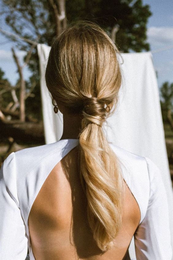 a classic low ponytail with a sleek top and hair wrapping the ponytail is a cool solution for a modern bride