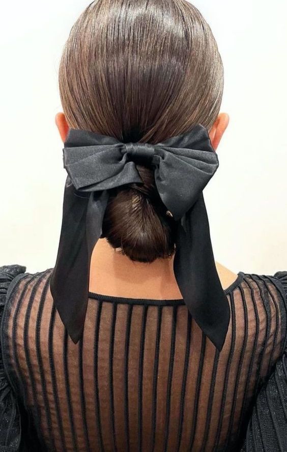a classic sleek low bun with a sleek top and a large black bow are a chic and cool combo to rock for a special occasion
