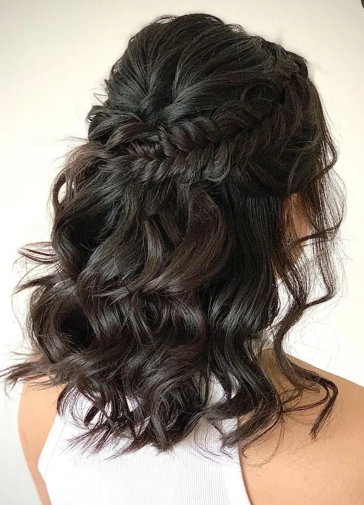 a classy half updo with a bump on top and a large braided halo plus curls down is a haristyle that always works