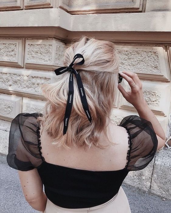a classy half updo with a messy top, waves and a black Chanel ribbon bow is amazing to make your look chic