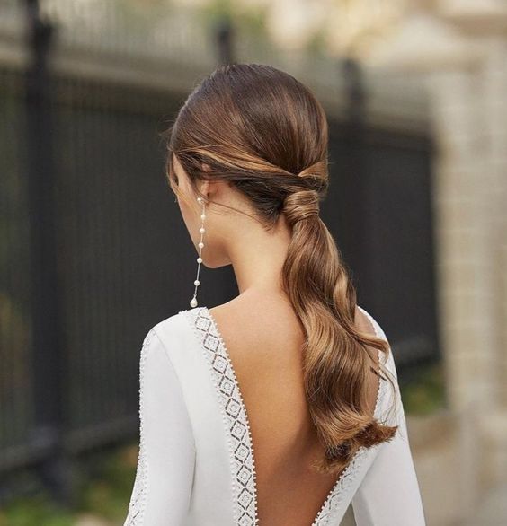 a classy low ponytail with waves and a sleek top is a stylish idea for a modern wedding