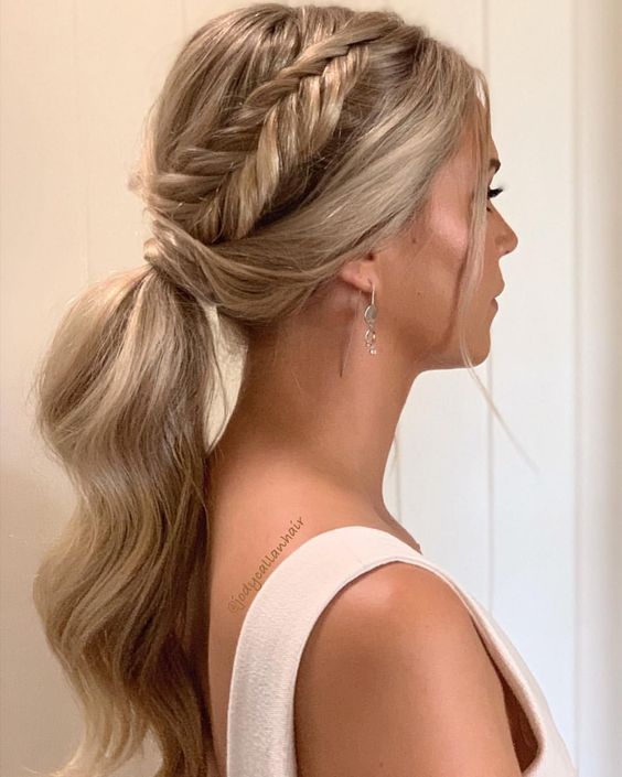 a classy low wavy ponytail with a braided halo and hair covering the ponytail is a cool and catchy idea