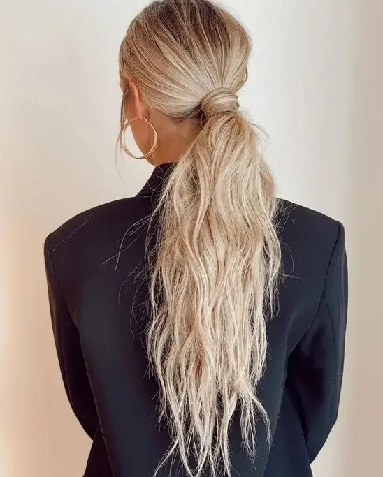a classy messy and textural low ponytail with a messy top and hair wrapping it is a cool idea for a modern bridal look