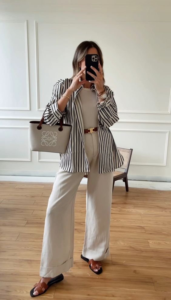 a classy spring outfit with a neutral top and trosuers, a striped button down, brown sandals and a small tote bag