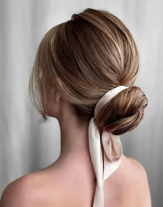 A classy wrapped low bun with a bump on top, a silk ribbon and face framing locks is a chic and stylish idea