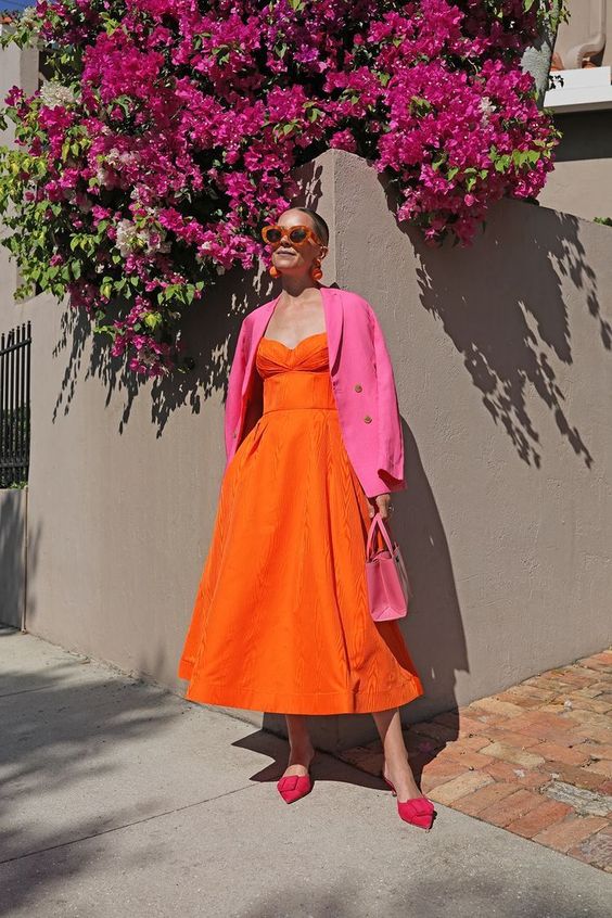 a colorful spring or summer wedding guest look with an orange midi dress, red shoes, a pink bag and a pink blazer