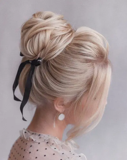 a cute wrapped top knot with a bump on top and face-framing hair plus a black ribbon bow for a trendy touch