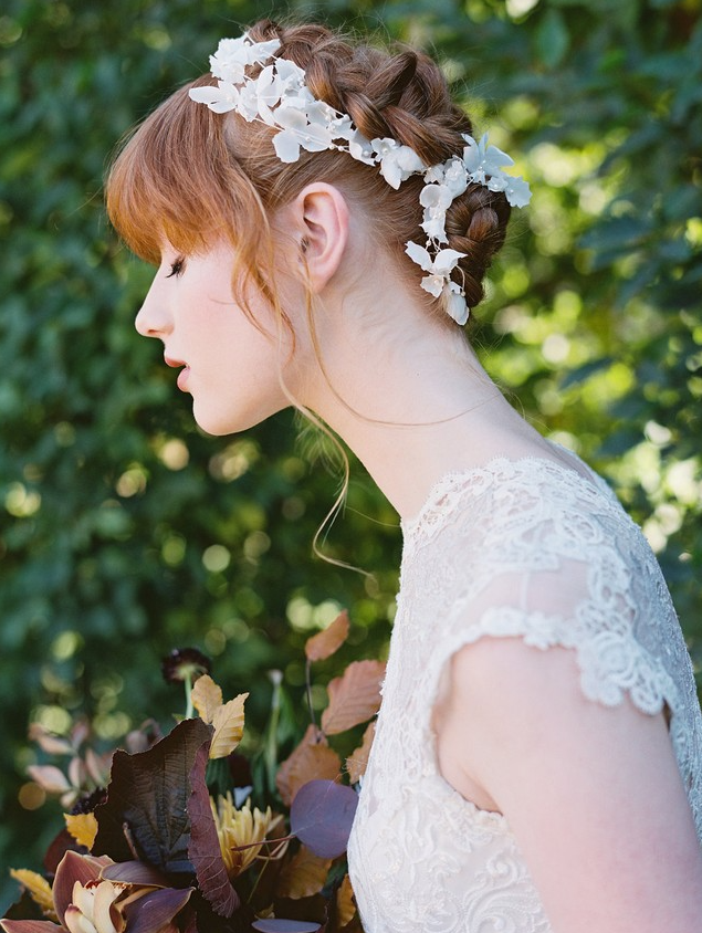 a fully braided updo with a white floral hair vine and bangs for a subtle and chic bridal look