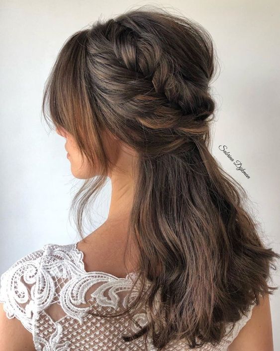 a half updo with a bump on top and a loose braided halo, face-framing bangs and textured hair down for a wedding