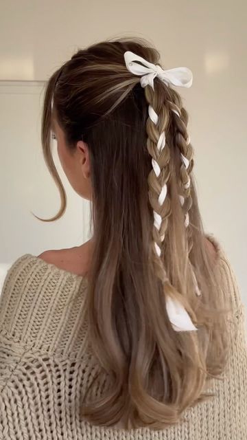 a half updo with braids with ribbon interwoven and a ribbon bow on top and face-framing hair is amazing for a girlish look