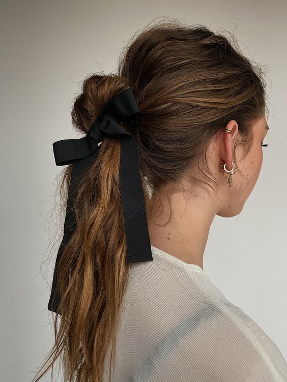 a high ponytail with a messy and volumetric top, a wavy messy ponytail and a black ribbon bow for an accent