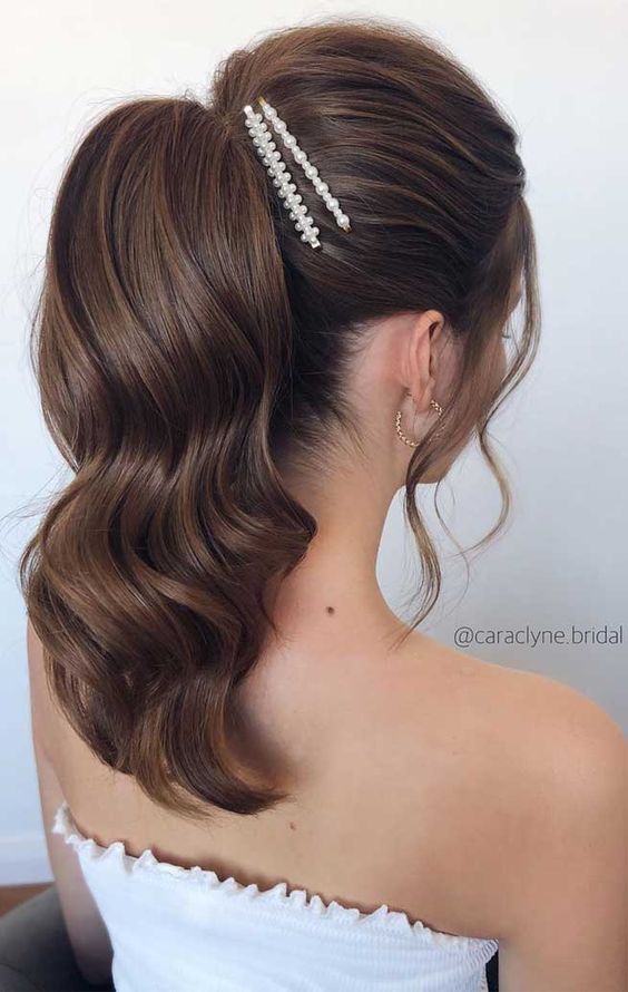 A high volumetric wavy ponytail with a volume on top and face framing hair plus pearl hair pins is amazing for weddings
