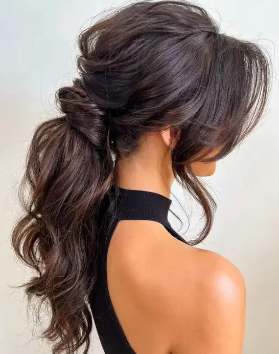 A jaw dropping wavy messy low ponytail with a messy volume on top, locks framing the face is amazing for a glam bride