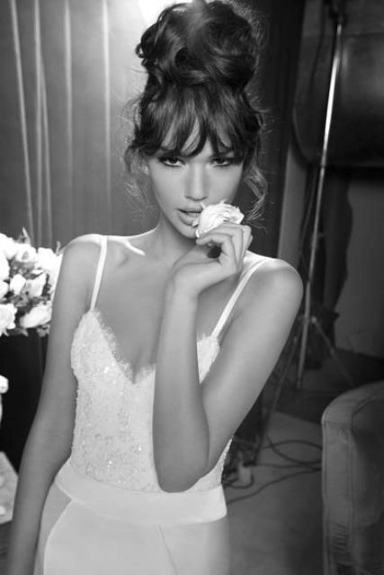 a large wavy top knot and classic bangs are a cool and cute combo for a glam and modern bride