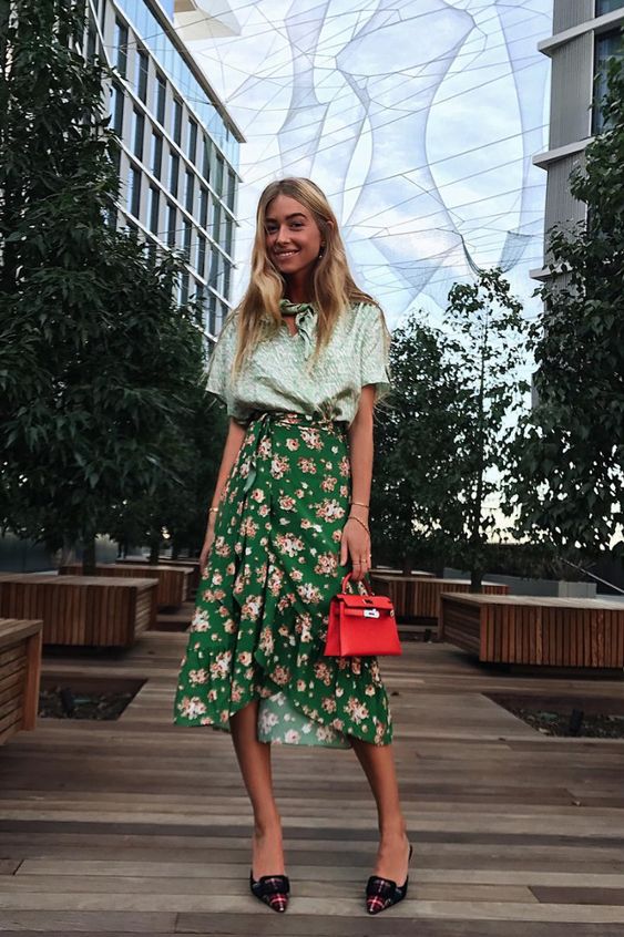 a light green blouse, a green floral midi skirt, mules and a bold red bag are a cool look for a bridal shower