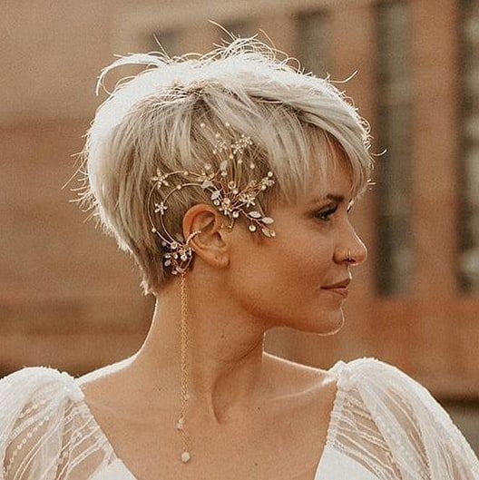 a long blonde pixie with bangs and a unique ear cuff with blooming coming on the hair and hanging down