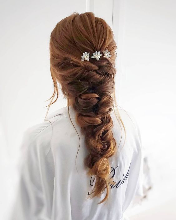a loose and thick braid with twists and some flowers is a chic and cool hairstyle for a bride