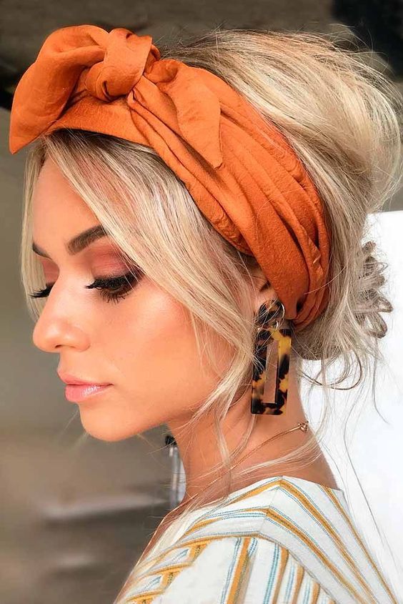 A lovely messy and volumetric low updo with a volume on top, face framing hair and a bold orange headband for a touch of color