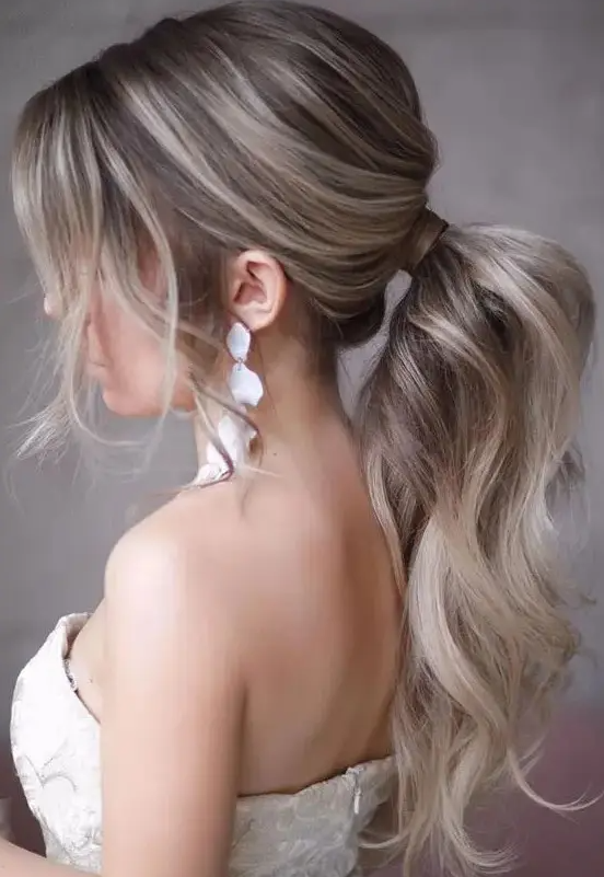 a lovely wavy and textural low ponytail with a bump on top and some locks framing the face is a chic idea to try