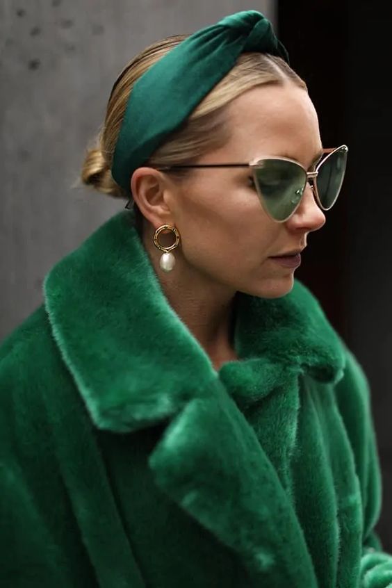 a low bun paired with a bold green headband that accents the faux fur coat and green eyewear