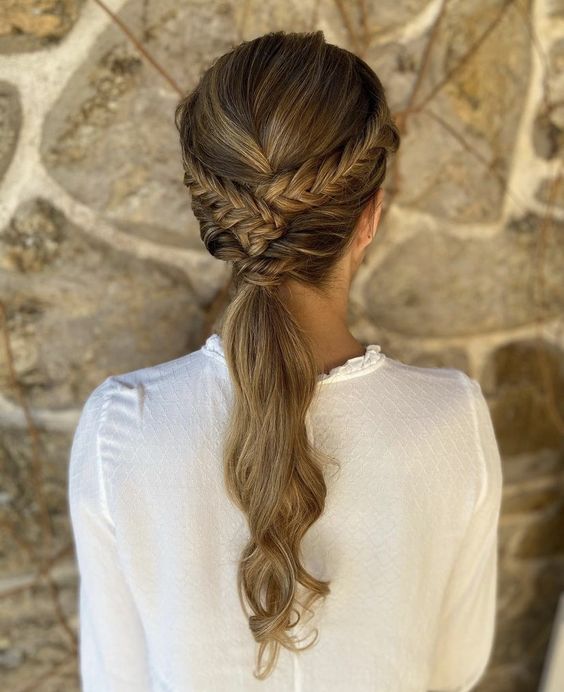 a low ponytail with a braided halo and a volume on top plus waves is a cool idea for a boho bride