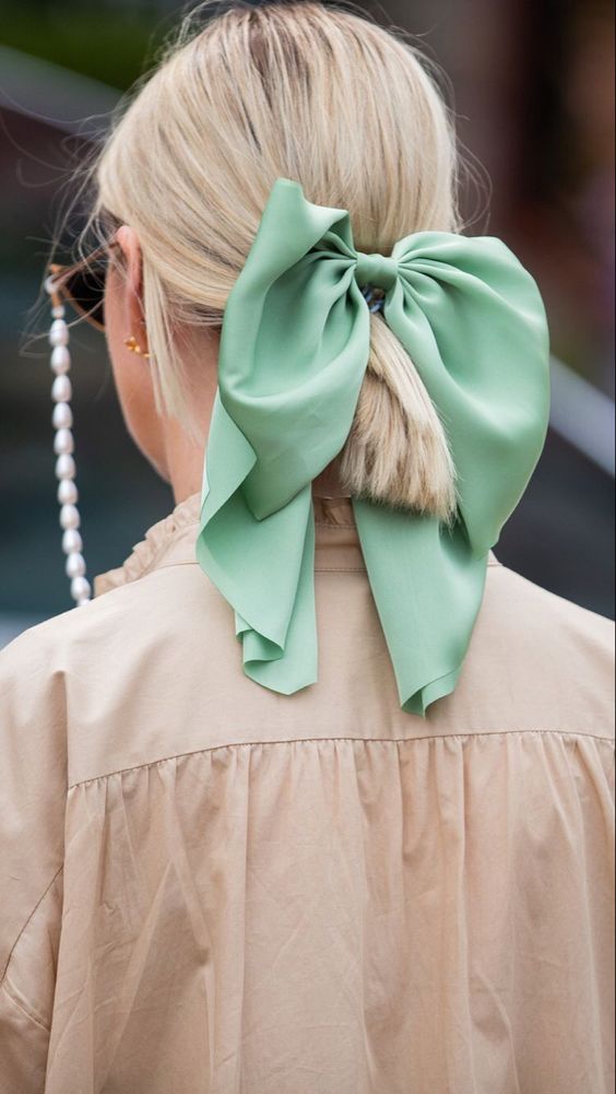 a low ponytail with a messy top and a mint green bow to accent the look and add color to it