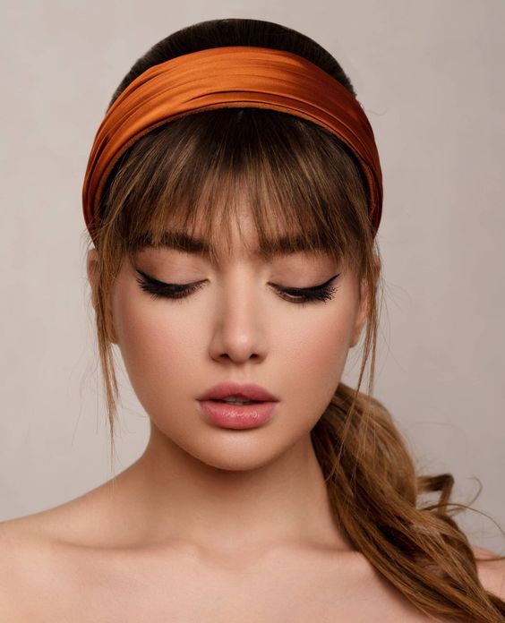 a low ponytail with a sleek top and layered bangs plus an orange satin headband are a cool combo to look wow