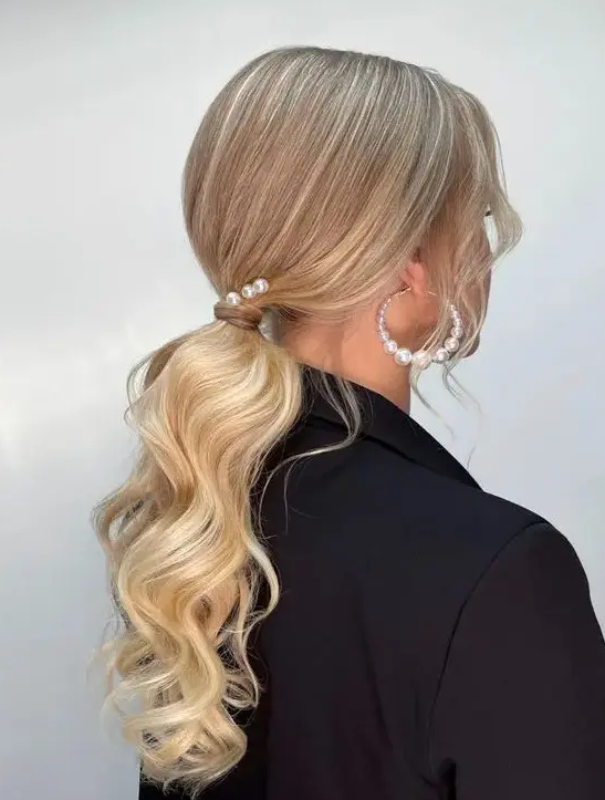 a low ponytail with waves, locks framing the face, some pearl pins and pearl earrings is a chic idea