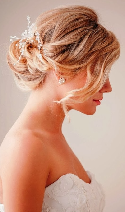 a low twisted chignon with a bump on top, a rhinestone hairpiece and long side bangs