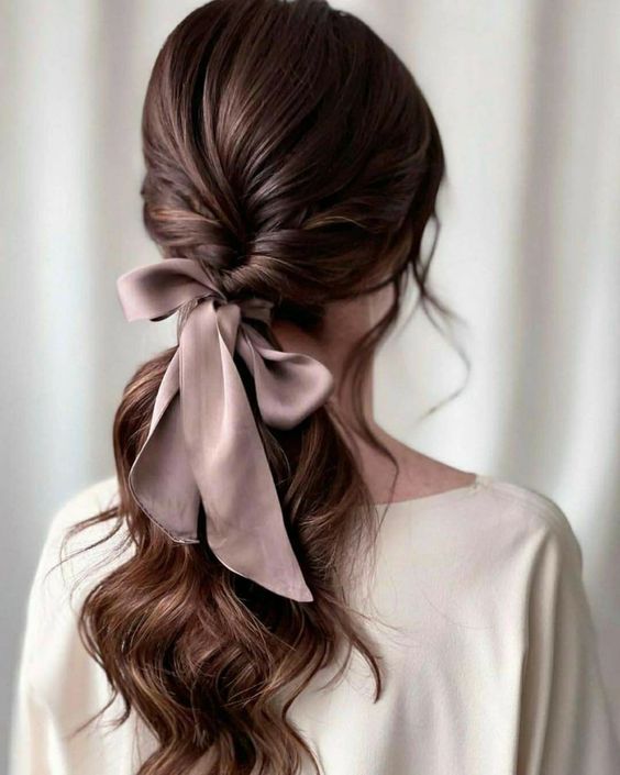 a low twisted ponytail with waves and a volume on top plus a lilac silk bow for a more chic and more elegant look