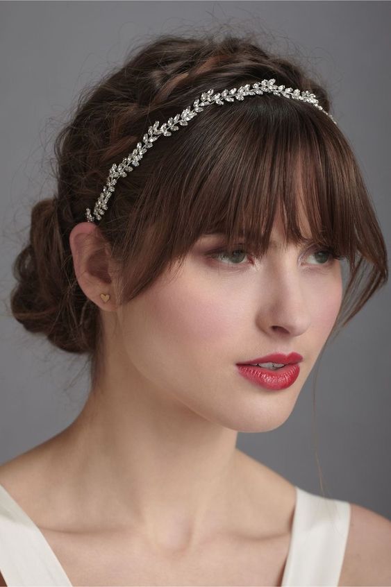 a low updo with a braided halo and a rhinestone headpiece plus layered bangs are great for a wedding