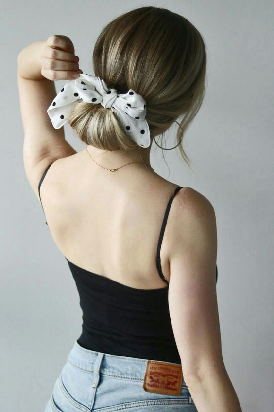 a low updo with a sleek top and face-framing hair plus a polka dot bow are a cool and playful combo to rock