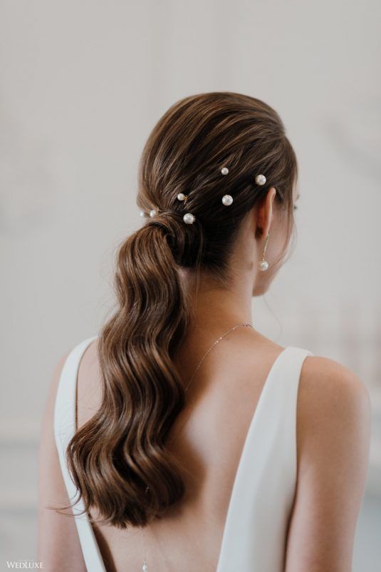 a low wavy ponytail with a sleek top and pearl hair pins is a chic and lovely idea for a modern glam bride