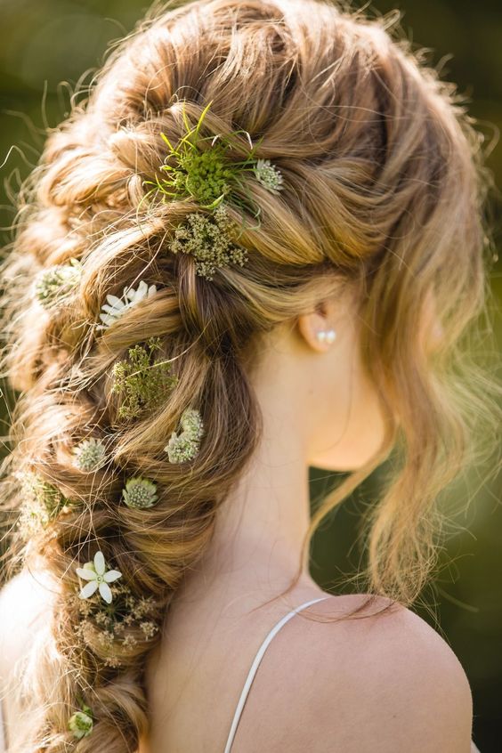 a messy and loose braid with greenery, white blooms and moss tucked in is a perfect woodland bridal hairstyle