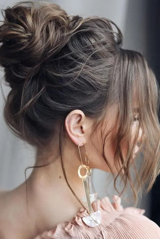 A messy and volumetric top knot with face framing locks is a catchy and cool idea for a glam and chic look