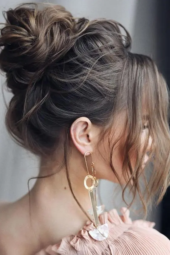 A messy and volumetric top knot with face framing locks is a catchy and cool idea for a glam bride