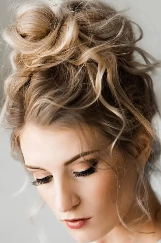 a messy and wavy top knot with a wavy top and some locks down is a cool and chic idea with effortless chic