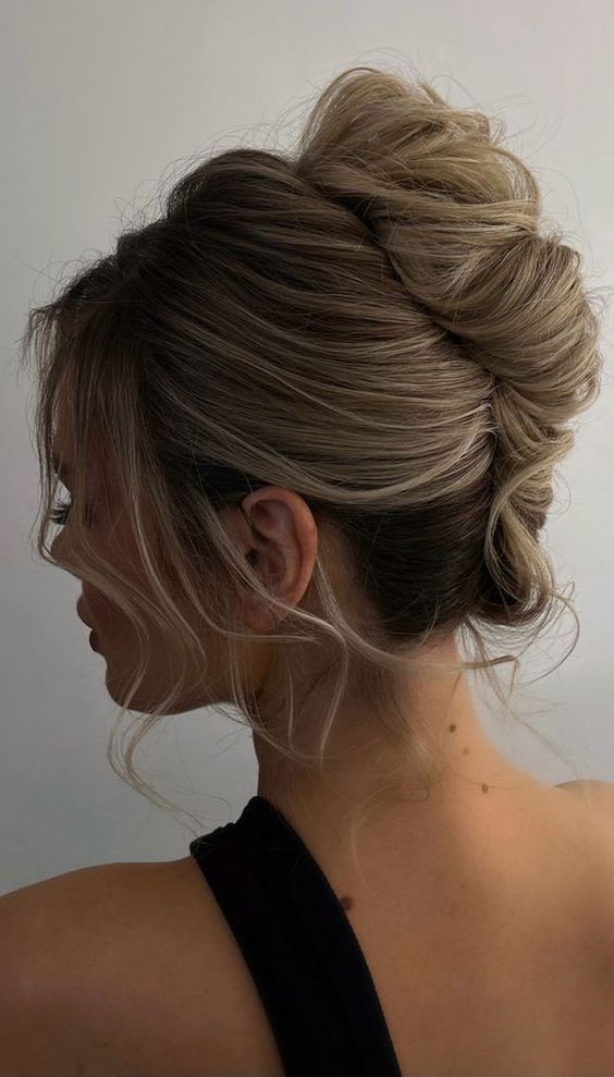 a messy chignon hairstyle with a voluminous top and bangs for a modern wedding