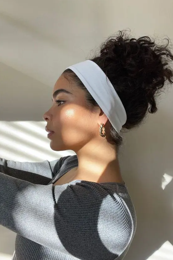 a messy curly bun on top, a sleek top and a white stretchy headband are a cool combo for every day, a look inspired by the 90s