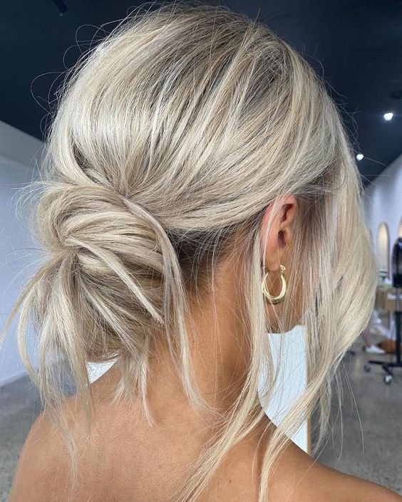 A messy low bun with a bump on top and face framing hair plus some hair out of the bun is a cool casual wedding hairstyle
