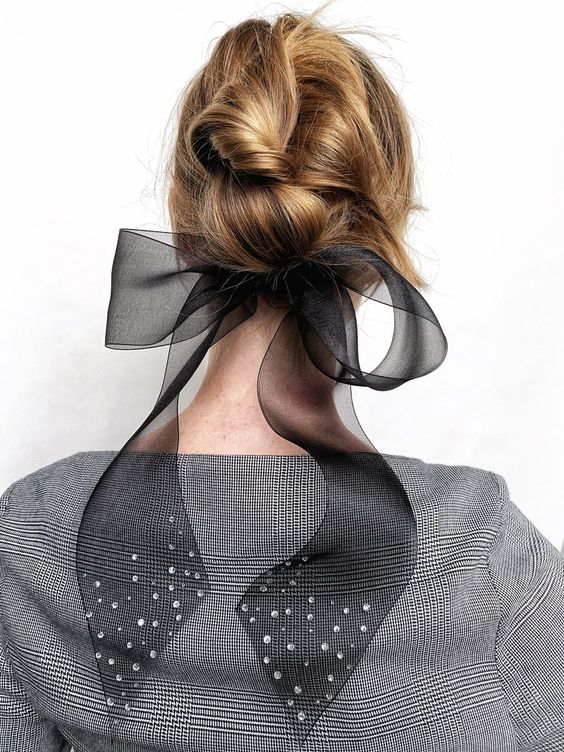 a messy low updo with twists and waves and a large black sheer bow are a lovely solution for a refined look