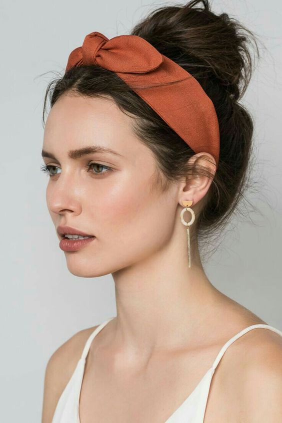 a messy top knot with a bold rust headband with a bow on top for a retro touch and a cool look