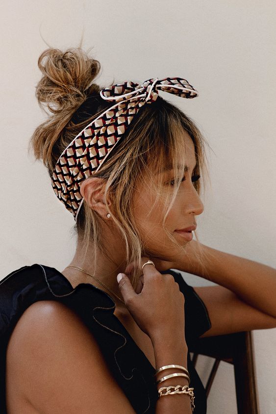 A messy top knot with a sleek top, face framing hair and a printed headband with a bow on top for a lovely retro look