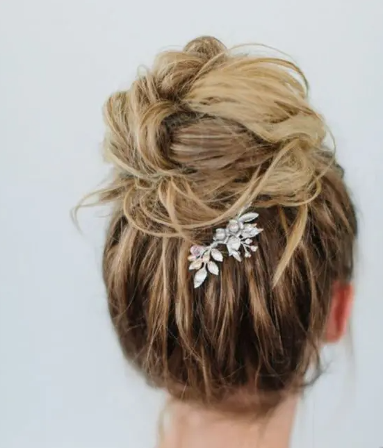 a messy top knot with a volume on top and a rhinestone hair piece is amazing for a chic bridal look