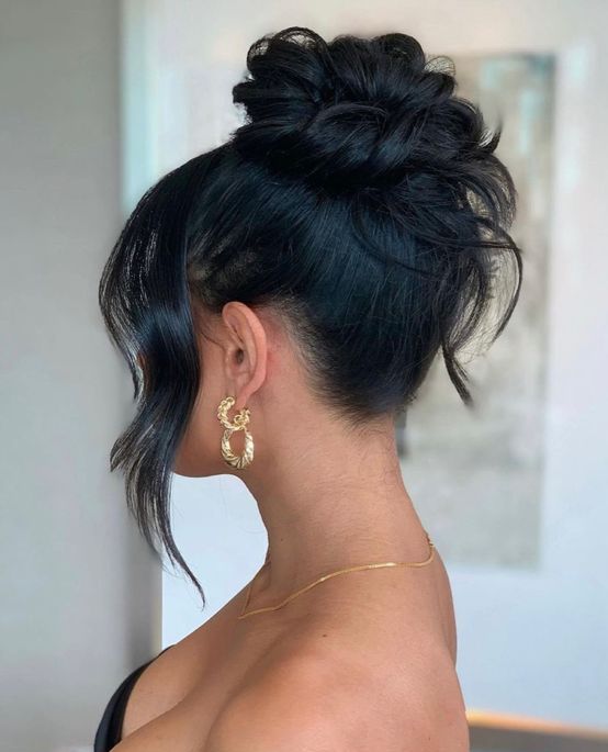 a messy wavy top knot plus a sleek top and side bangs are a glam and chic hairstyle for medium wavy hair