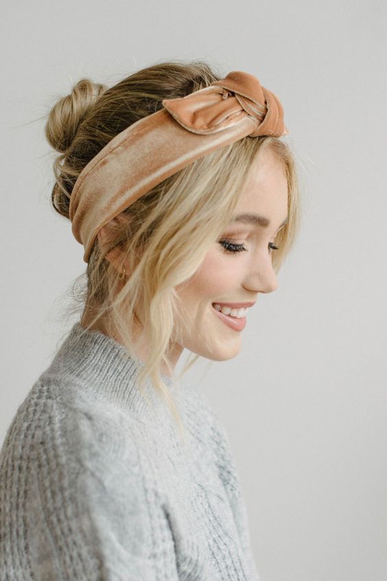 a midi bun with a volumetric top and wavy hair framing the face and an orange velvet headband for a touch of color