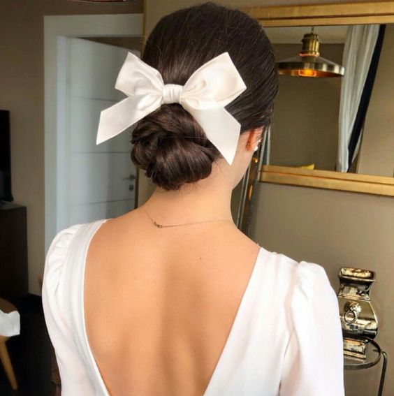 a pretty wrapped low bun with a sleek top and an elegant white bow that brings sophisticattion to the look