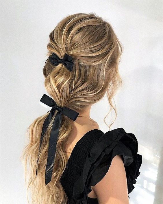 a refined party hairstyle with a ponytail and a volume on top, waves down plus a couple of black bows is amazing