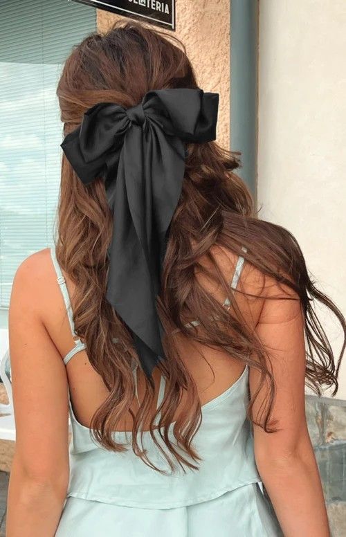 a romantic wavy half updo with a messy top and waves down plus a large black bow for an accent are amazing