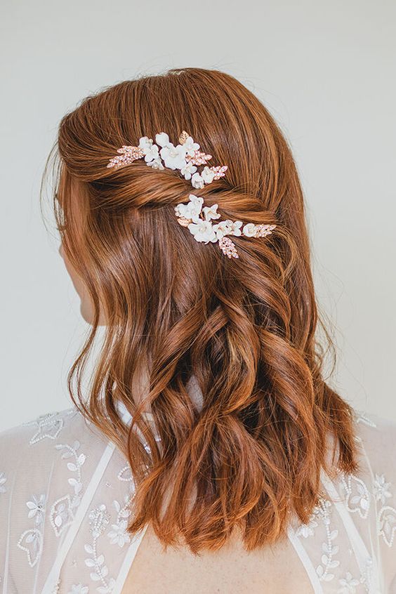 a simple and chic half updo with some some hair secured to the side of the head with a floral hair piece and waves down